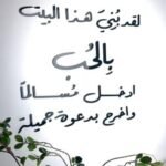 منحوتة أكريليك باللون الأسود، تحمل عبارة ترحيبية مزخرفة مع تفاصيل نباتية خضراء.