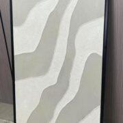 لوحة جبس بتصميم مميز بألوان رمادية وبيضاء، مع تفاصيل منقوشة، بإطار أسود أنيق.