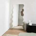 مرآة جدارية بتصميم عصري، ذات حواف متموجة، بلون فضي، تضيف لمسة أنيقة لأي مساحة داخلية.