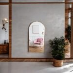 مرآة جدارية بتصميم قوسى، إطار ذهبي، تعكس الألوان الدافئة في غرفة أنيقة.