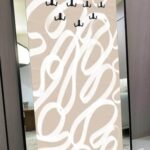 لوحة فنية مزودة بمرايا وعلاقات، بتصميم عصري وألوان دافئة، إطار أسود مع خطوط بيضاء على خلفية بيج.
