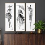 مجموعة من ثلاث لوحات فنية بالأبيض والأسود تُظهر تصاميم أزياء أنيقة، بإطار ذهبي.